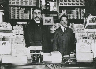 874824 Portret van winkelchef H.A. Wimmers met zijn knecht Jopie, achter de toonbank in de winkel van de Koninklijke ...